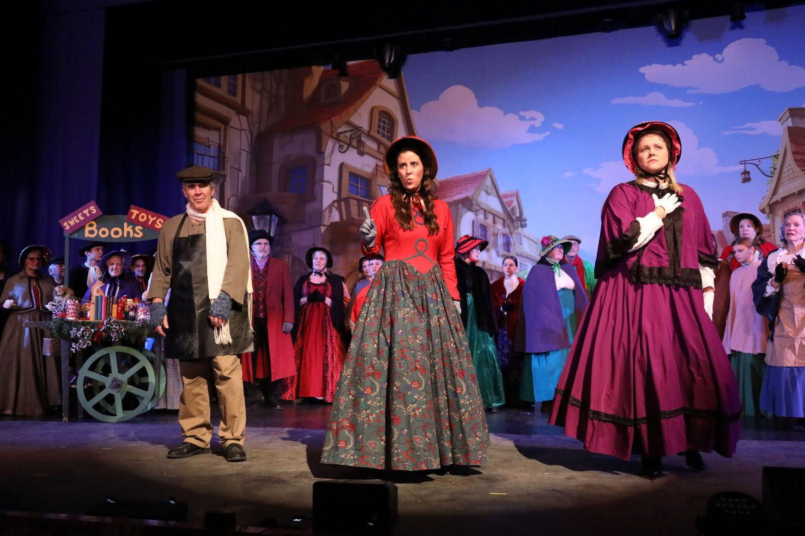 Men and women in Dickens costumes gather in a town square scene.