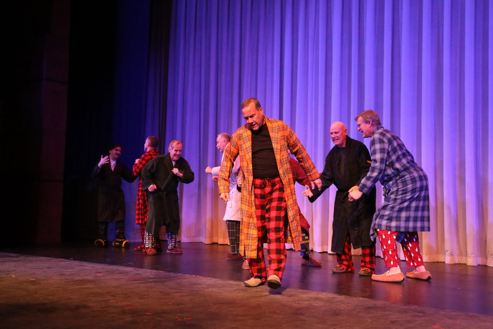 Middle-aged men dressed in bathrobes dance.