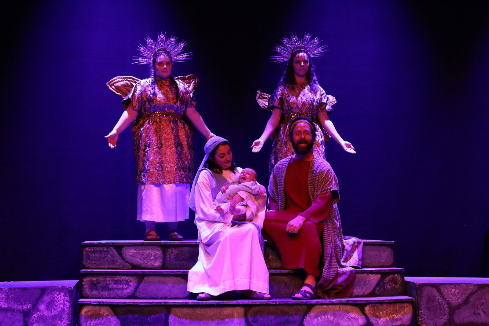 Mary holds baby Jesus with Jospeh seated next to them with angels on either side.